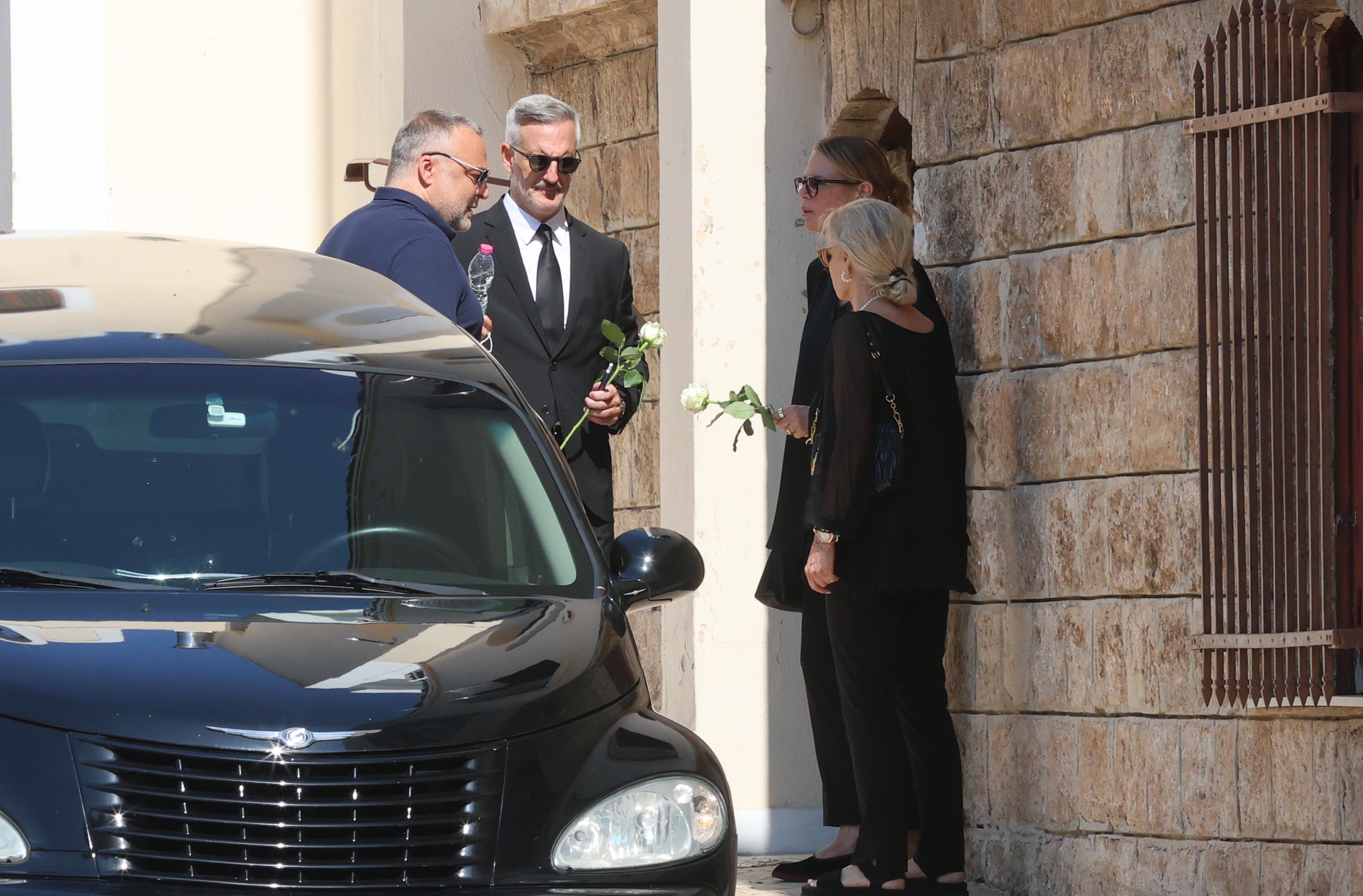 Ντυμένη στα μαύρα και κρατώντας ένα λευκό τριαντάφυλλο, η Έλενα Κατραβά έφτασε στον ναό για να αποχαιρετήσει τον σύζυγό της.
